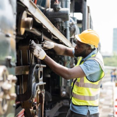 African American male engineer maintenance locomotive engine in locomotive repair garage. Male railway engineer use wrench repair train wheel in train garage