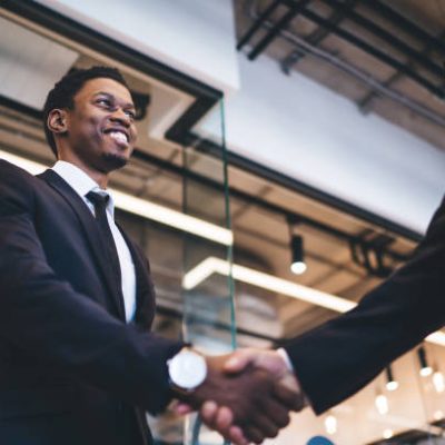 From below glad young African American male in formal suit finding employment at office and shaking hands with faceless hirer