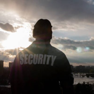A black male security guard in uniform watching over the street from the high floor.
